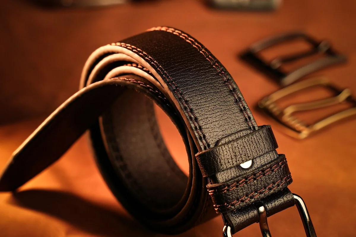 Black leather belt with orange stitching, coiled, with a silver buckle in the foreground